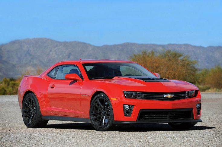 a red chevrolet camaro is parked in the desert