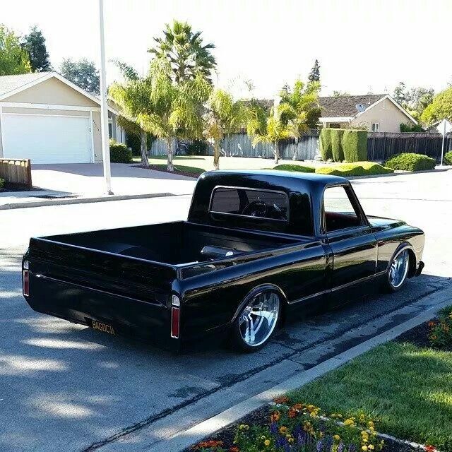 a black truck parked on the side of a road next to a flower bed in front of a house