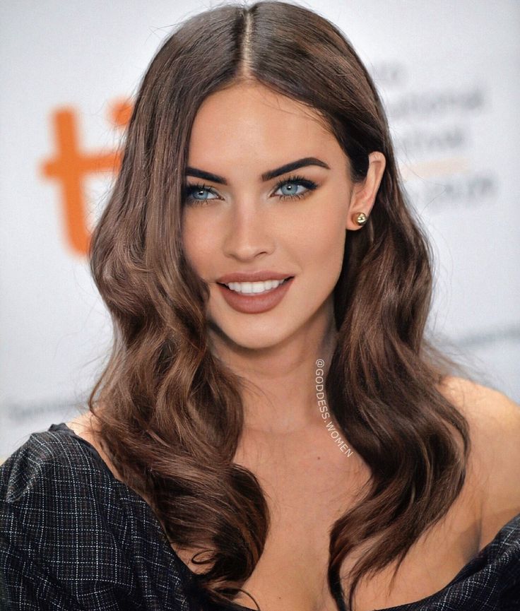 a woman with long brown hair and blue eyes wearing a black dress is smiling at the camera