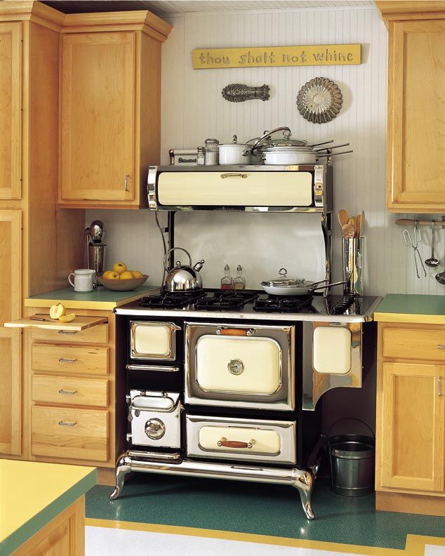 an old fashioned stove in the middle of a kitchen with wooden cabinets and green flooring