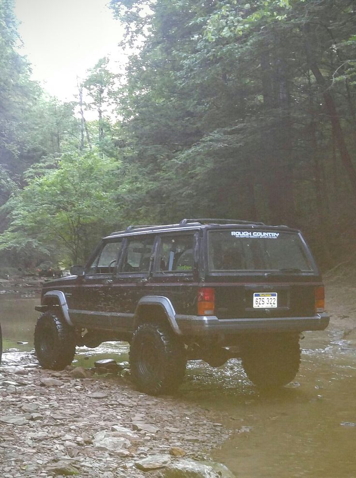 a black jeep is parked in the mud near some trees and water with its wheels off