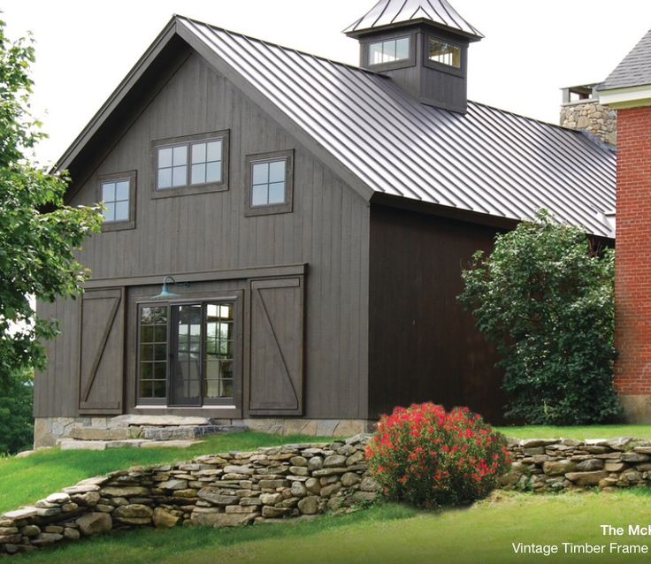 a barn style house with a metal roof and stone wall around the front yard area