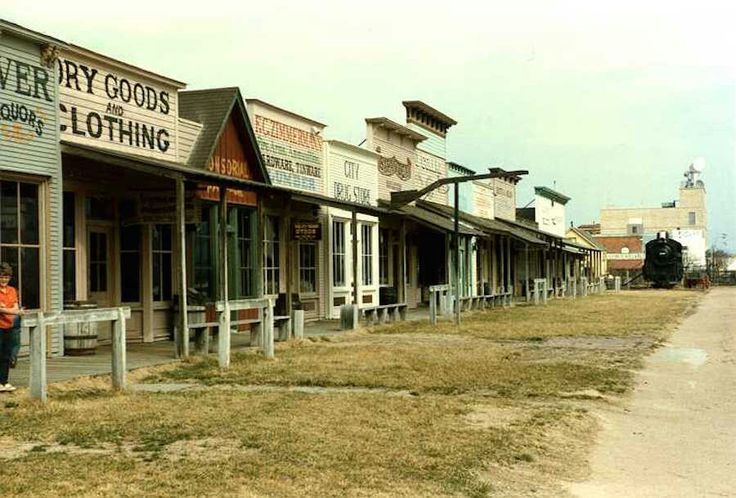 a man standing in front of a row of old store fronts on the side of a road