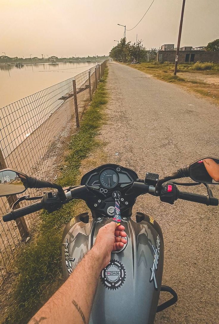 a person riding on the back of a motorcycle down a dirt road next to a body of water