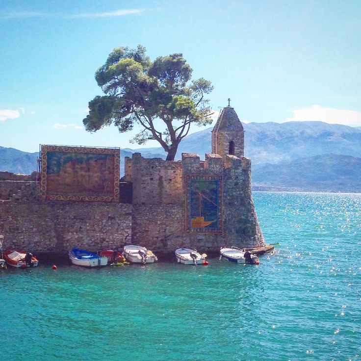 there are many small boats in the water near a stone wall with a tree on top