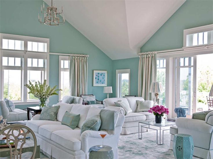 a living room filled with white furniture and lots of windows covered in shades of blue