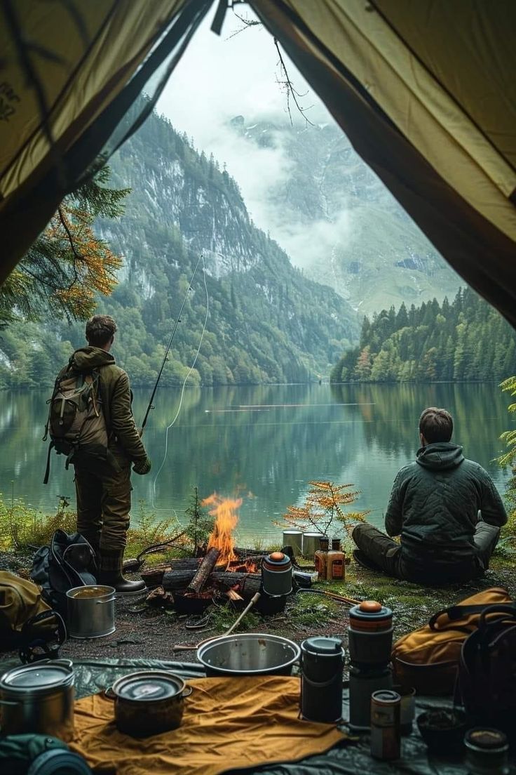 two men are sitting around a campfire in the mountains with their backpacks on