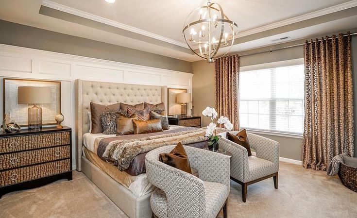 a bedroom with a large bed and two chairs in front of the window, along with a chandelier