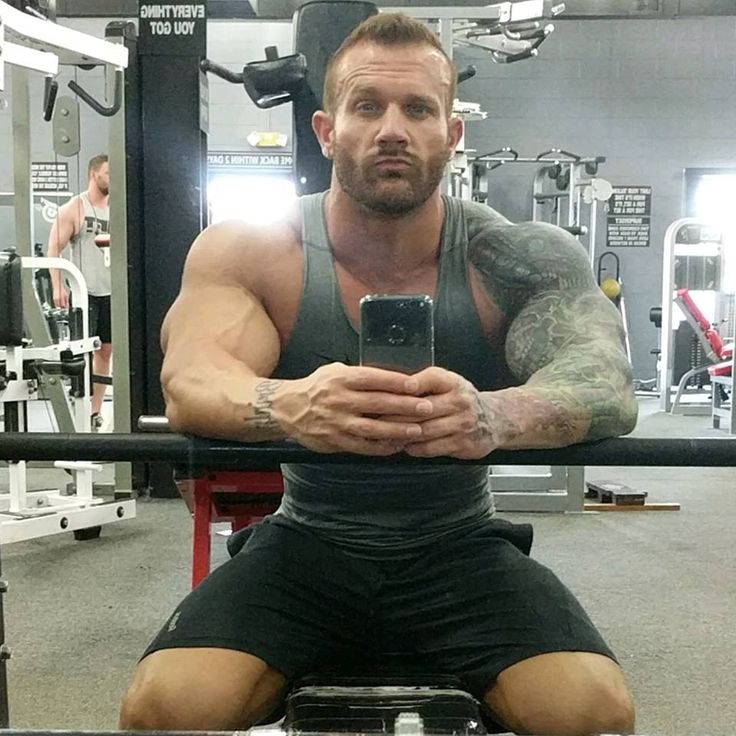 a man sitting on top of a bench in a gym holding a cell phone up to his face