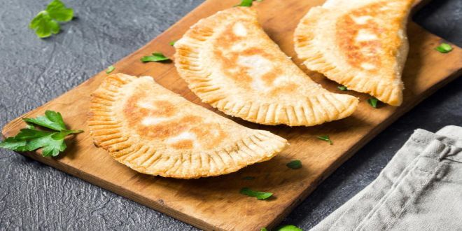 three empanada pies on a cutting board with parsley sprigs