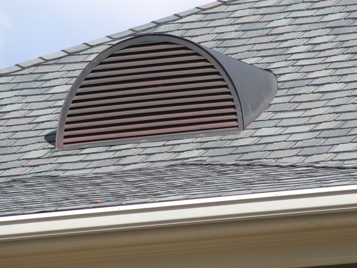 an arched window on the roof of a house with shingles and a sky background