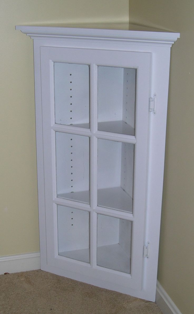 a white cabinet with four glass doors in a corner by a wall and carpeted floor