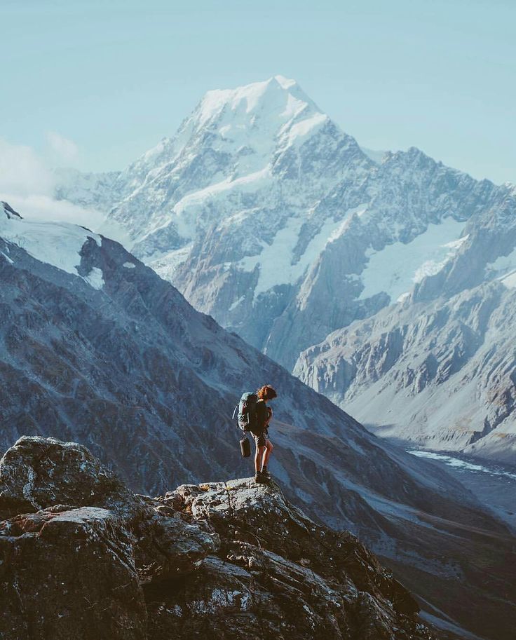 a person standing on top of a mountain looking at the snow covered mountains in the distance