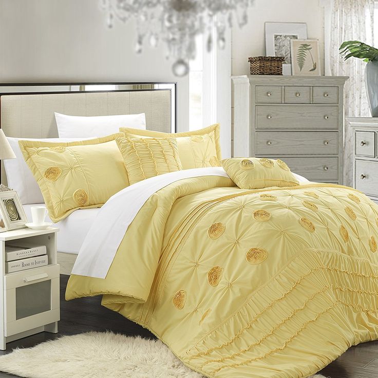 a bed with yellow comforter and white sheets in a room next to a chandelier