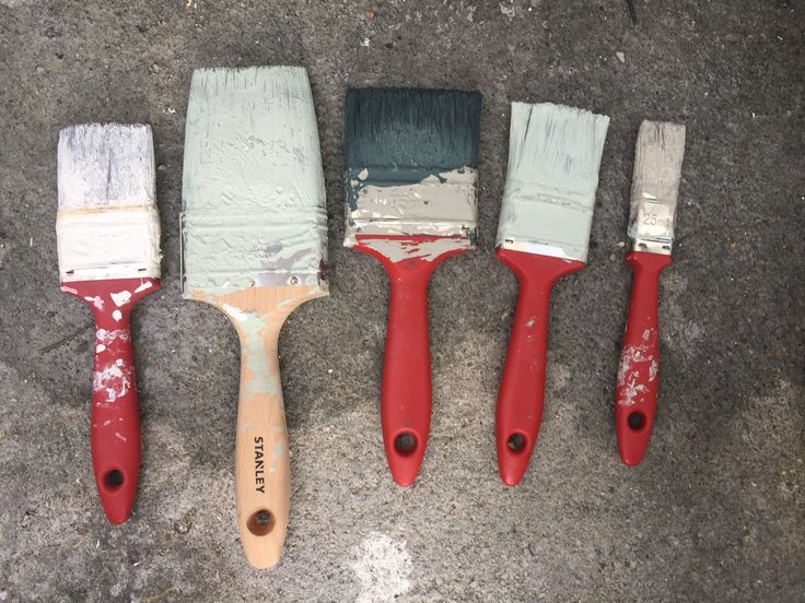 five paint brushes lined up in a row on the ground with one painted red and one white