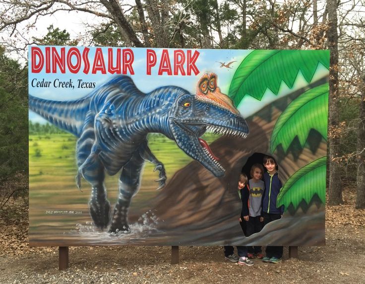 two children standing in front of a dinosaur park sign with an image of a t - rex