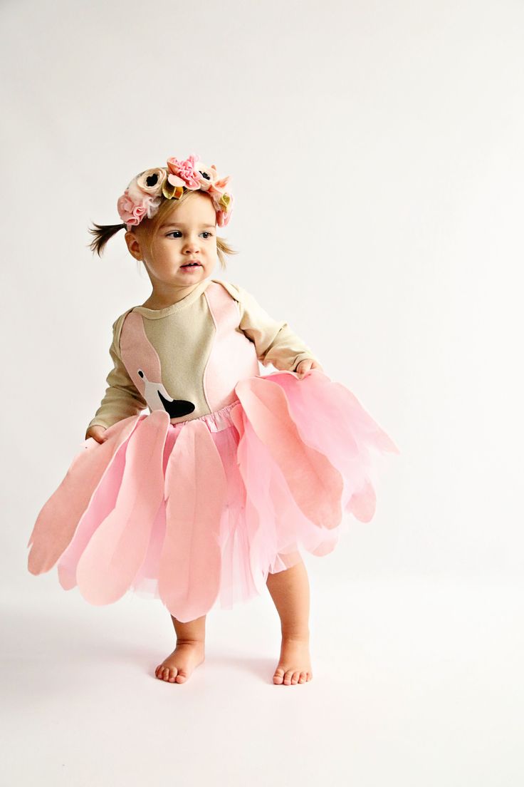 a baby girl wearing a pink tutu and headband, standing in front of a white background