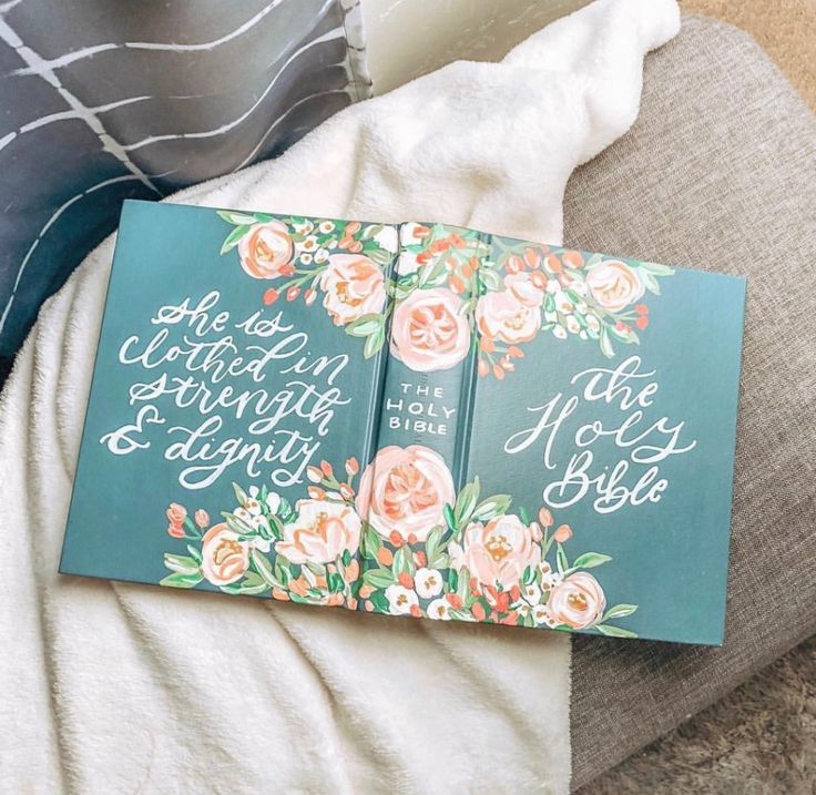 an open book sitting on top of a couch next to a blanket and pillow with flowers