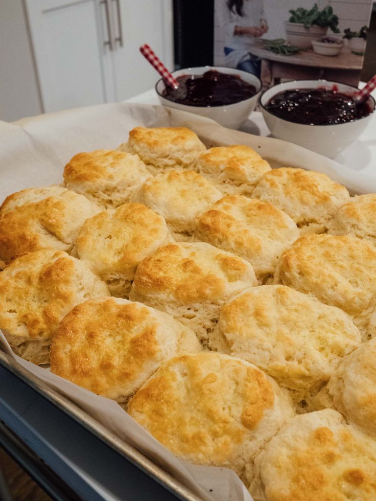 a baking pan filled with biscuits next to two bowls of jam on a counter top