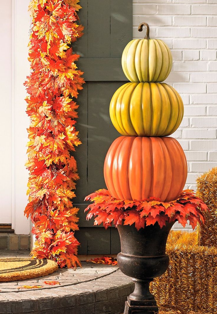 pumpkins are stacked on top of each other in front of a house with fall foliage