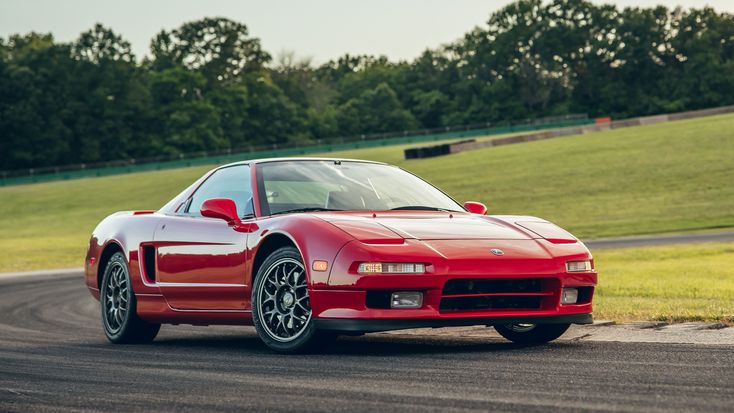 a red sports car driving on a track near some grass and trees in the background