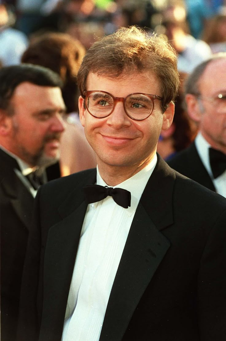 a man in a tuxedo and bow tie smiles for the camera at an event