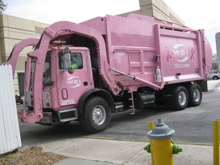 a pink garbage truck parked next to a yellow fire hydrant in front of a building