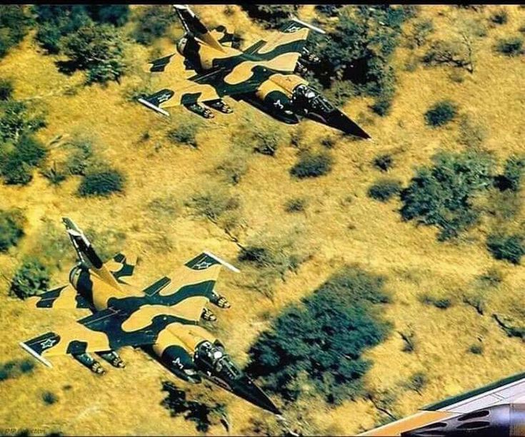 an aerial view of several fighter jets flying in the sky over trees and grass,