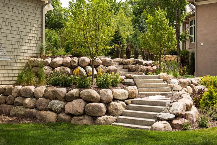 a stone wall next to a house with steps leading up to the front door and landscaping