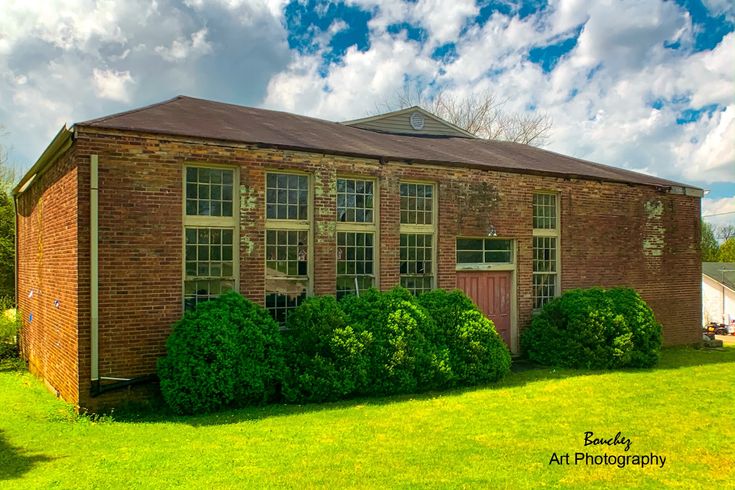 an old brick building surrounded by lush green grass and bushes on a sunny day with clouds in the sky