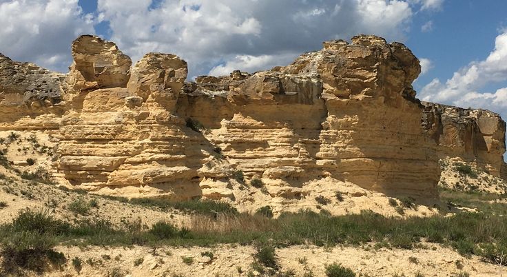 some very big rocks in the desert with grass and bushes on the ground near by