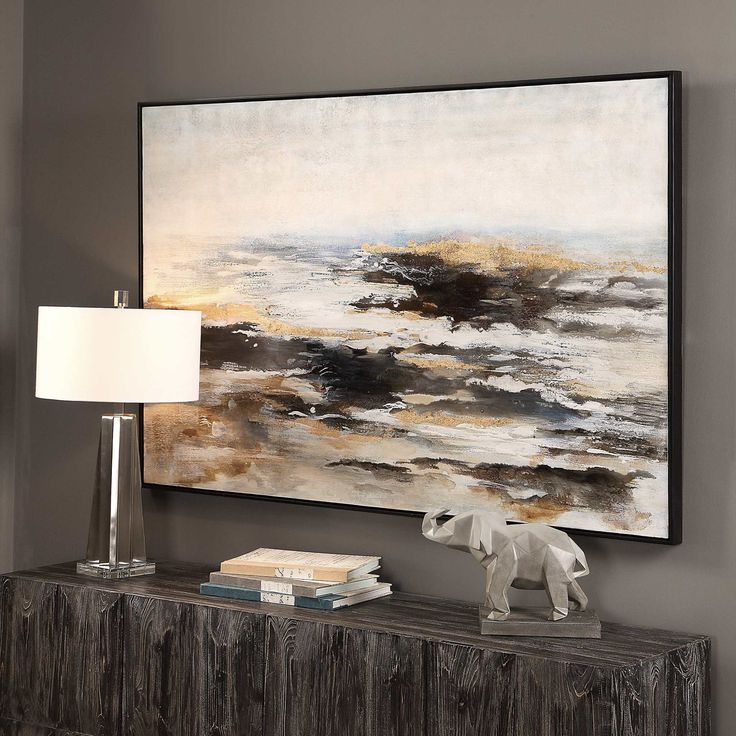 a large painting hangs on the wall next to a table with a lamp and books