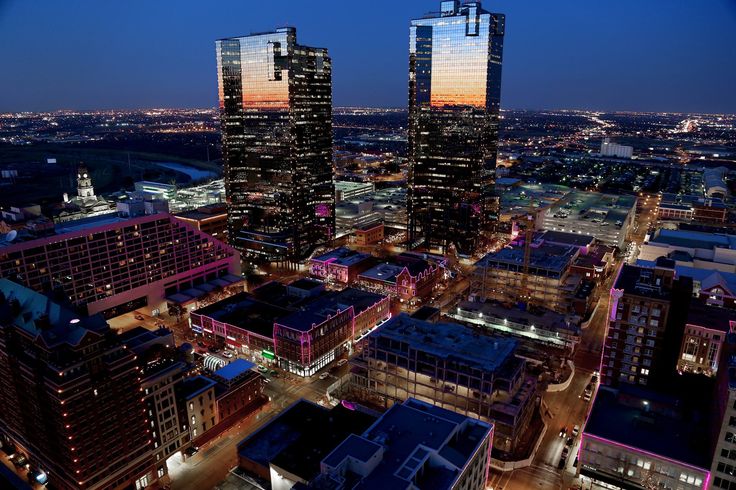 an aerial view of some very tall buildings in the city at night with lights on