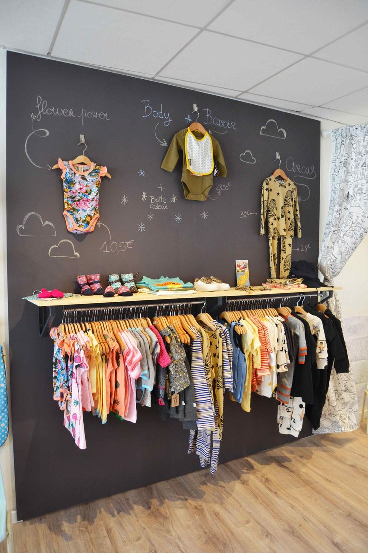 a blackboard with clothes hanging on it next to a shelf filled with baby ones