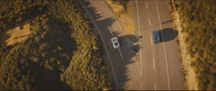 two cars driving down a road next to trees