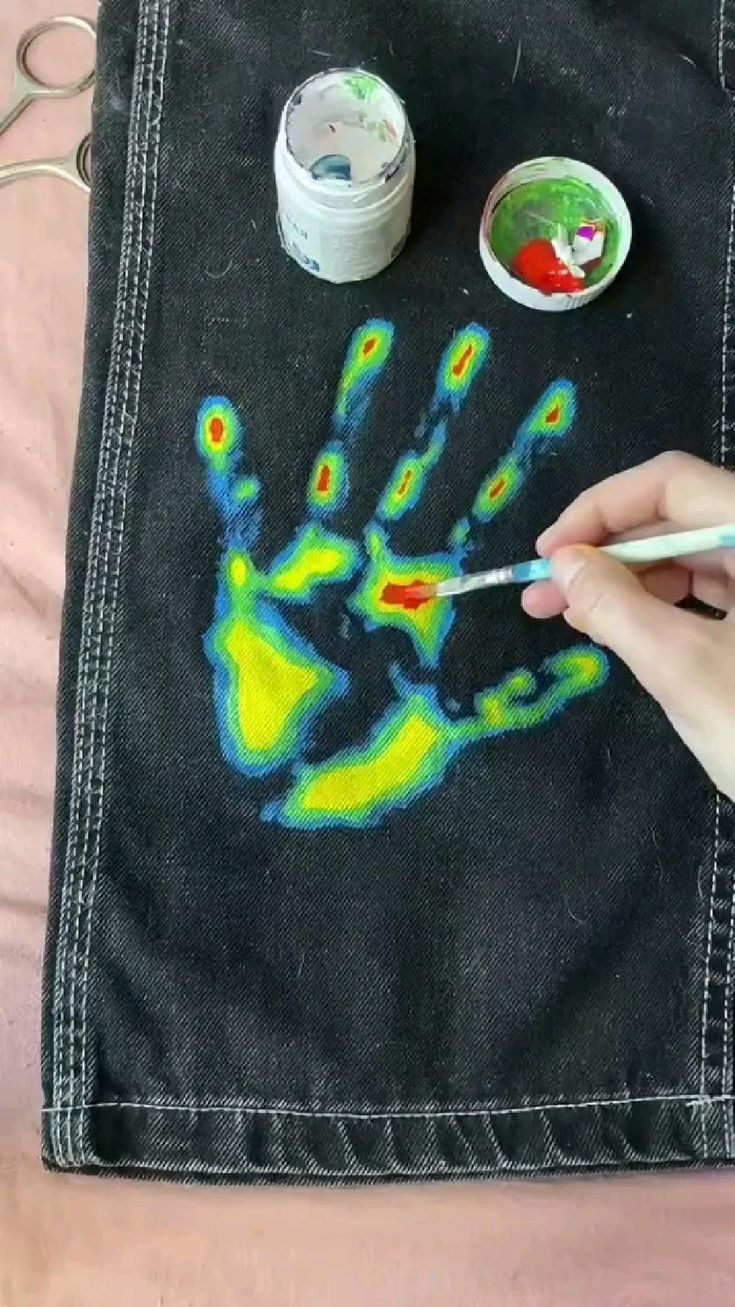 someone is painting their hand on a black piece of cloth with yellow and blue paint