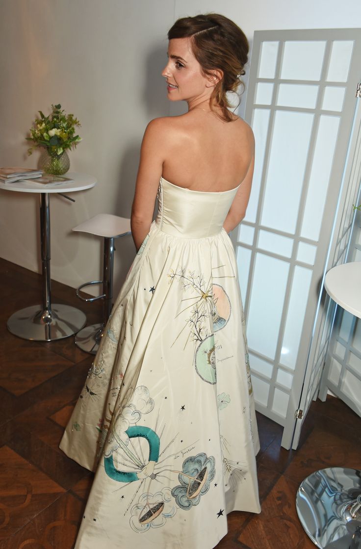 a woman standing in a room wearing a dress with flowers on it and looking off to the side