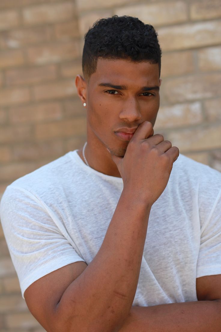 a young man standing in front of a brick wall with his hand on his chin