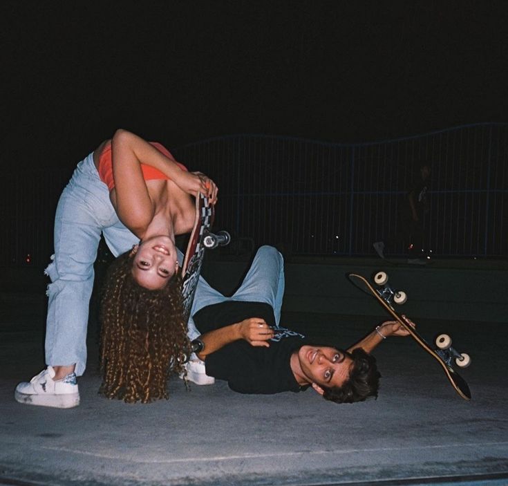 two women are laying on the ground with their skateboards and one is holding her head