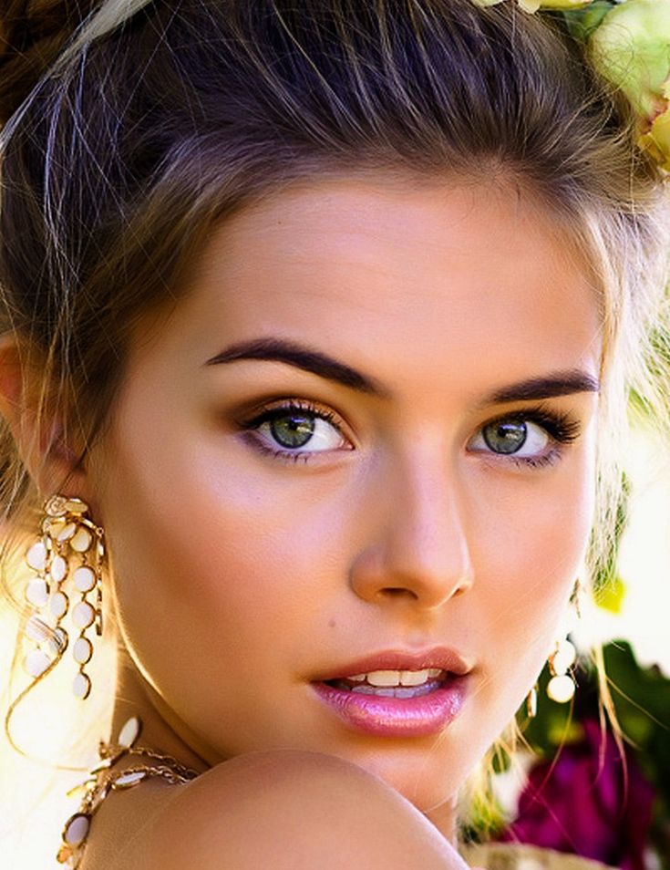 a beautiful young woman with blue eyes and flowers in her hair is posing for the camera