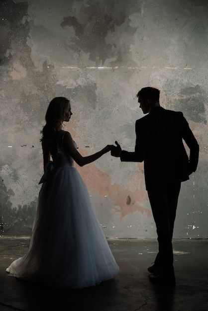 a man and woman standing next to each other in front of a dirty wall holding hands