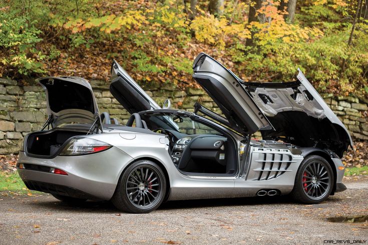 a silver sports car with its hood open and it's door opened on the road