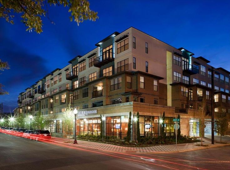 an apartment building lit up at night on the corner of a street with cars passing by