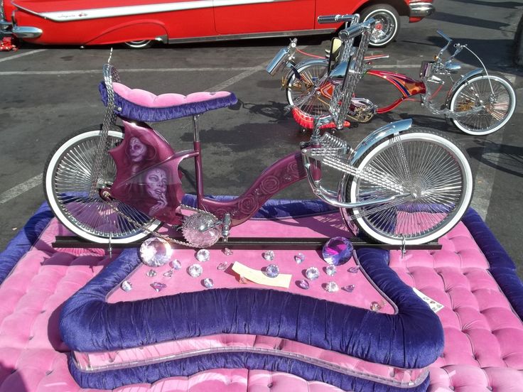 a pink and purple bike is parked in a parking lot with other bikes behind it