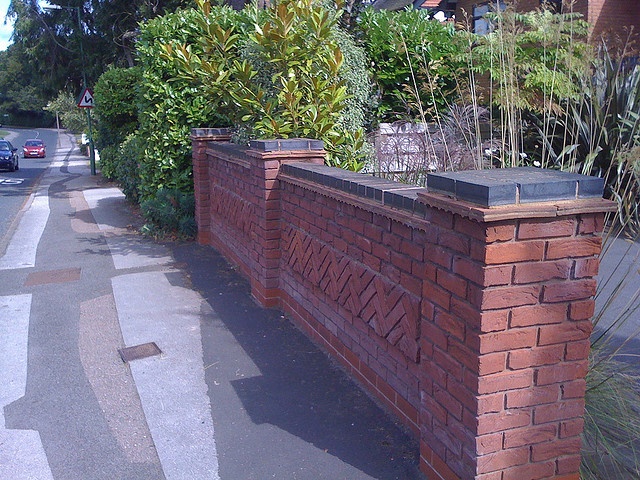 a brick wall with plants growing on it next to a street in front of a house