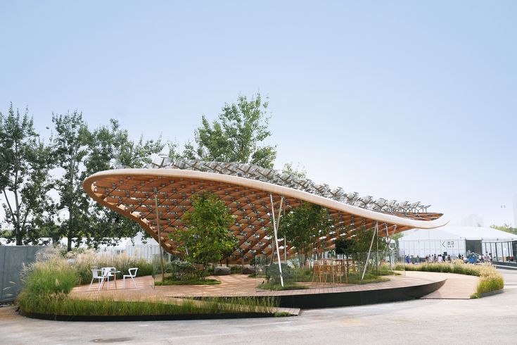 an artistically designed pavilion sits in the middle of a parking lot, surrounded by trees and bushes