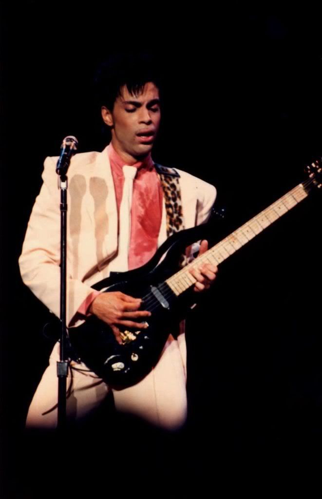 a man in white suit and tie playing an electric guitar with microphone on black background