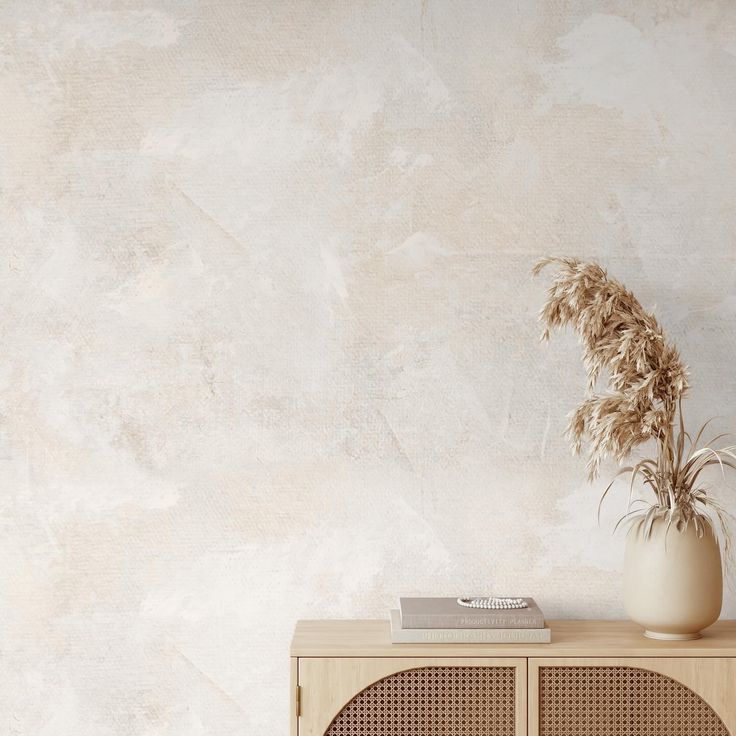 a white vase sitting on top of a wooden cabinet next to a wall with a plant in it