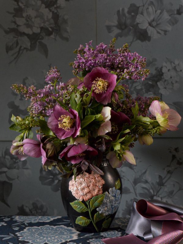 a vase filled with lots of purple flowers on top of a blue table cloth next to a wall