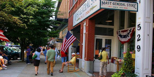 many people are walking down the sidewalk in front of some shops and buildings with flags on them